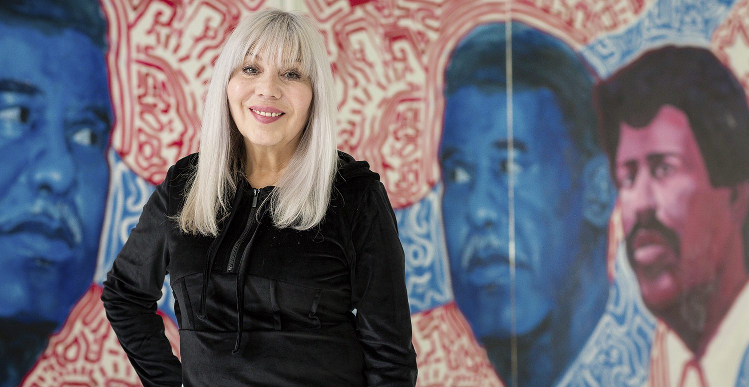 Organizer and pastor Emma Lozano, wearing a black hoodie, poses in front of a mural that depicts Chicago mayor Harold Washington and Lozano’s brother, Rudy Lozano.