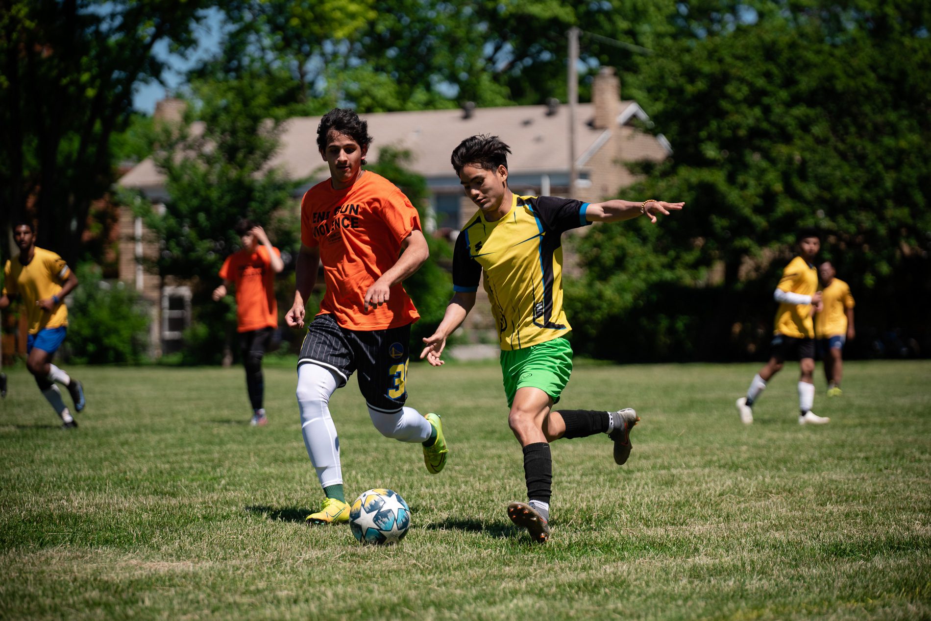 two soccer players fighting over the ball; one with orange jersey and the other with yellow jersey