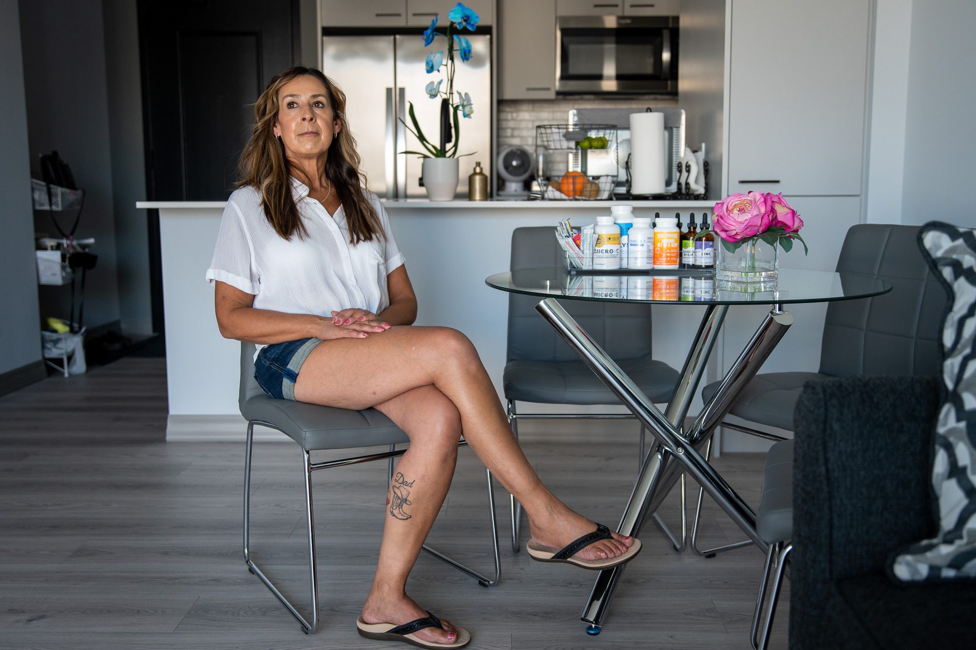 Ester Escamilla Hughes in jean shorts and a white top sitting next to a glass table in her home